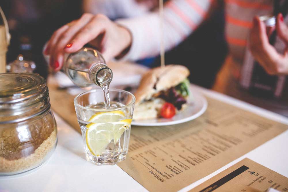 Restaurant patron pouring water at a dining table with a printed paper menu, illustrating the durability and everyday use of restaurant menu paper.