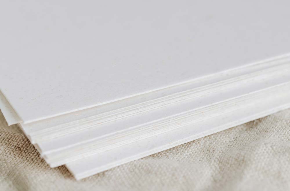 Close-up of stacked white fiber cardstock showing the edges and thickness of multiple sheets.